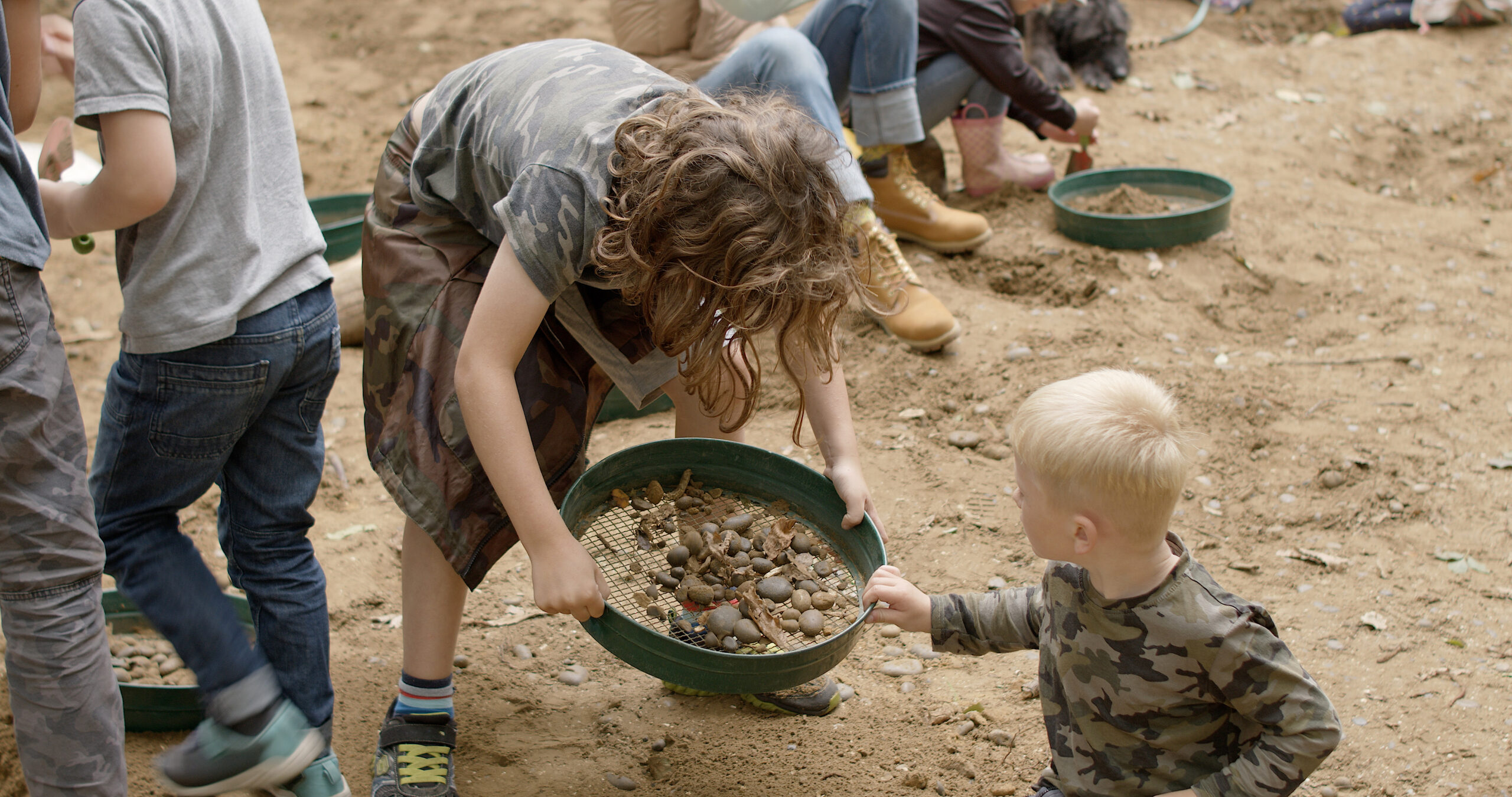 two children using a sieve to hunt for fossils