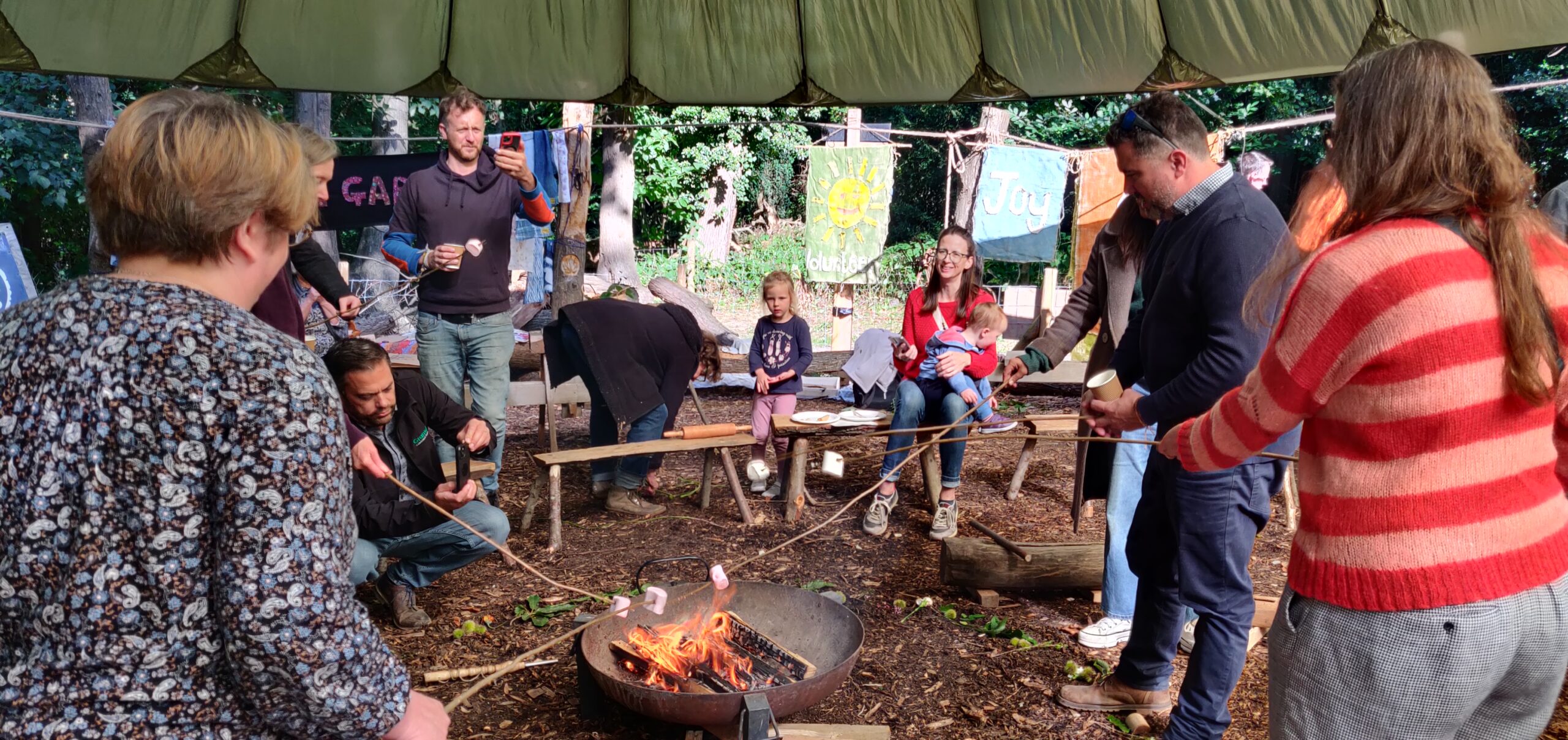 4 people standing toasting marshmellows around a fire