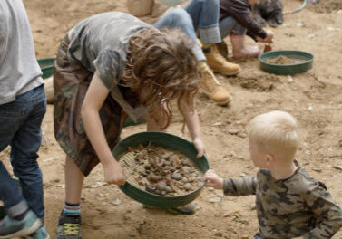 two children using a sieve to hunt for fossils