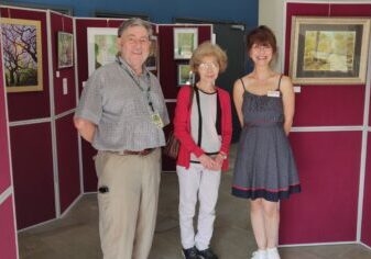 3 adults standing in front of an art exhibition