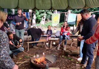 4 people standing toasting marshmellows around a fire